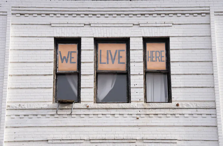 Signs in an apartment window spell out We Live Here.