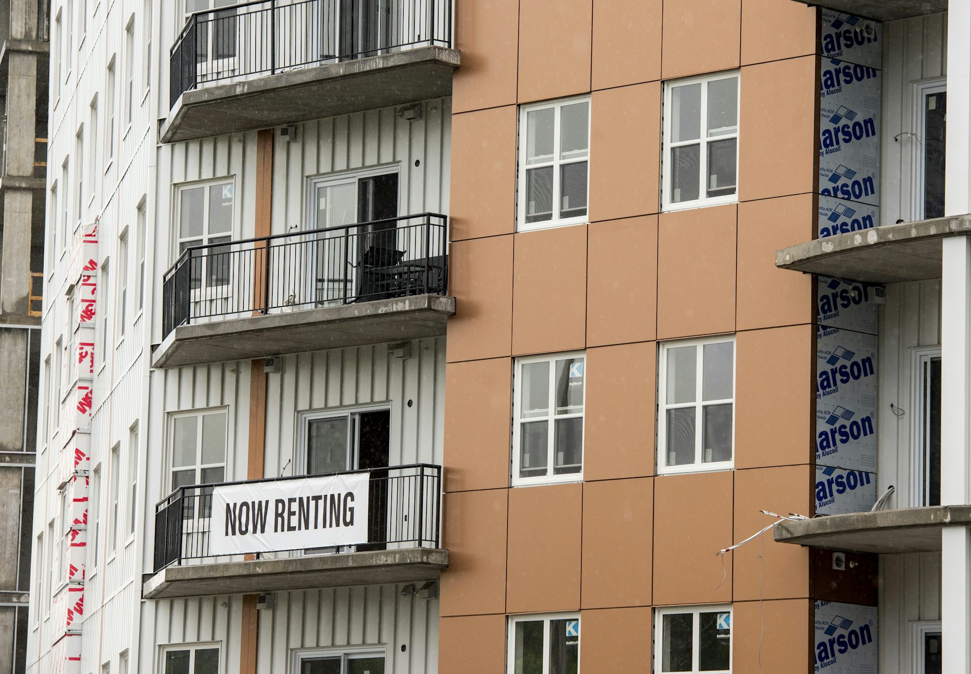 A sign that says 'now renting' hangs on the balcony of an apartment building