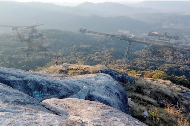 View of mountains and trees with a faded helicopter and rifle superimposed in the top half