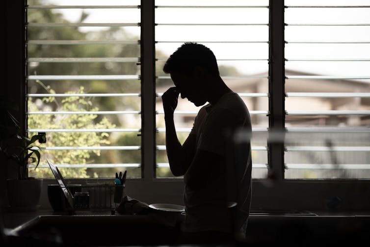Young man in silhouette against window, one hand on forehead