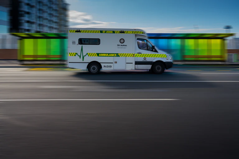 Ambulance driving in front of coloured bus stop.