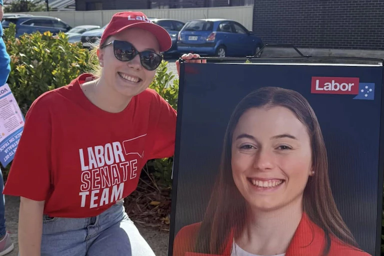 A young woman smiles next to her campaign sign for the senate