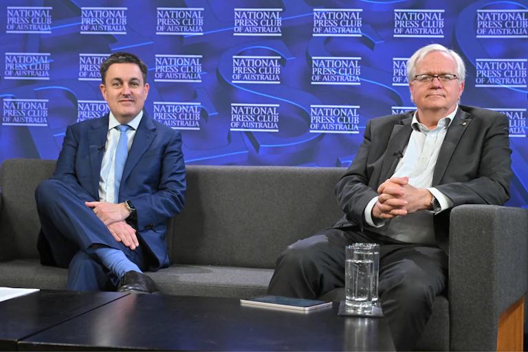 Professors Richard Holden and Brian Schmidt sit on a couch on the press club stage.