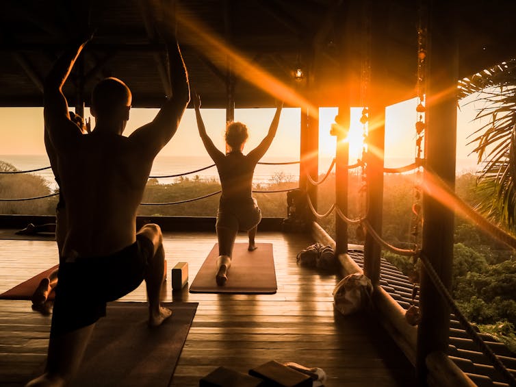 Several people in silhouette doing yoga as the sun sets