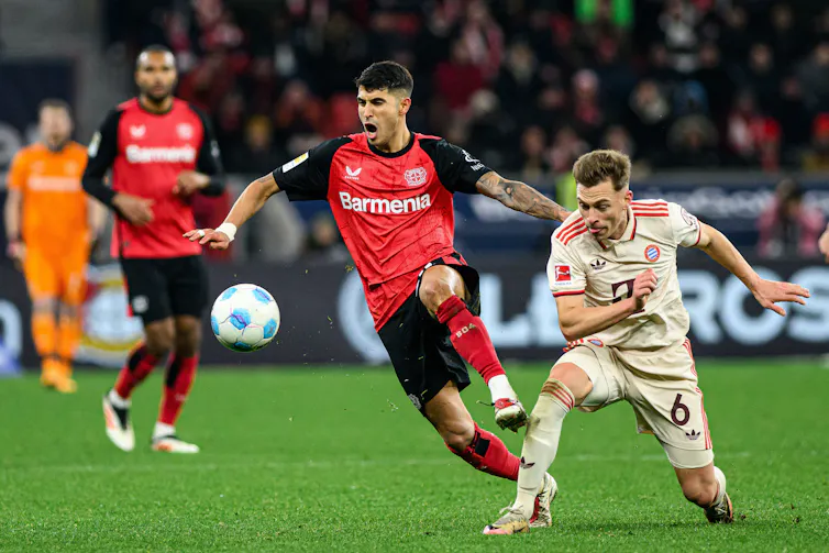 Two football players from opposing teams face off on the pitch as they chase the ball.