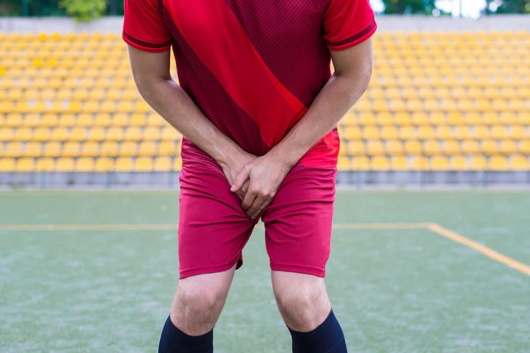 A man in a football uniform protects his groin with his hands.