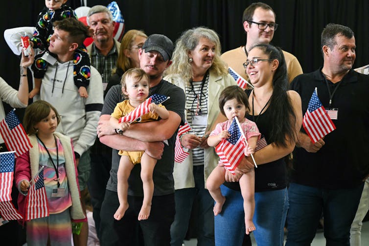 A group of white people hold small children and American flags and stand together.