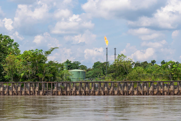 Tanque y chimenea con fuego rodeados de vegetación a la orilla del río Amazonas