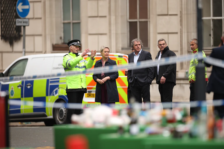 Behind police tape, an officer explains the scene to Cooper, Rotheram and others