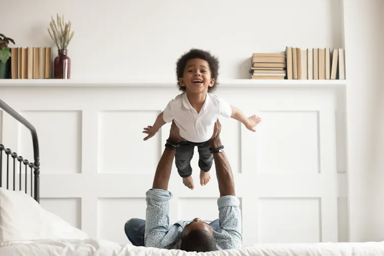 A man lying on a bed lifting a toddler above his chest