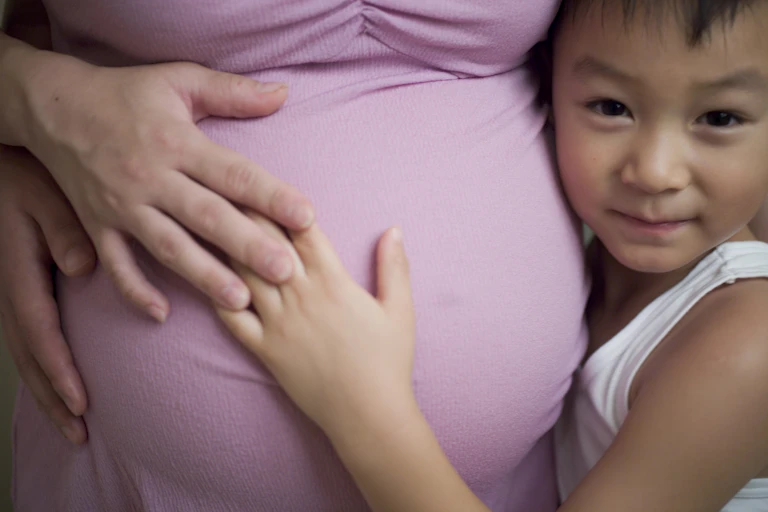 Young boy with his face against his mother's pregnant belly