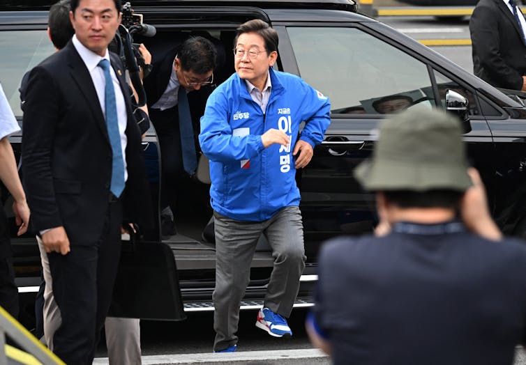 A man in a blue jacket runs out of a car.