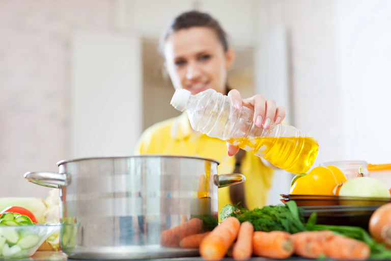 Mulher em uma cozinha colocando óleo em uma panela no fogão