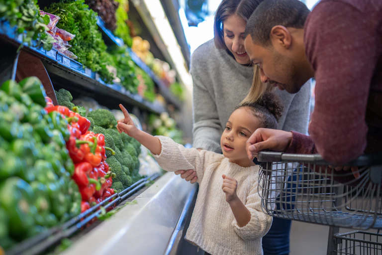 Parents and preschool age girl in the grocery store produce aisle.