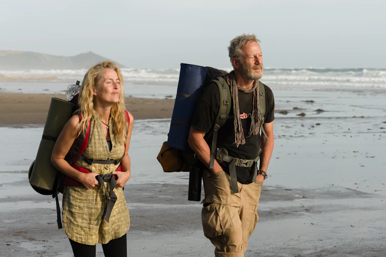 Gillian Anderson as Raynor Winn and Jason Isaacs as Moth Winn walking on a beach