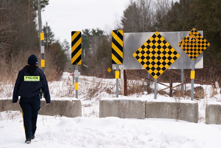 Un oficial de policía en la nieve en la nieve hacia la frontera cruzó con varios signos amarillos y negros de peligro a su alrededor.