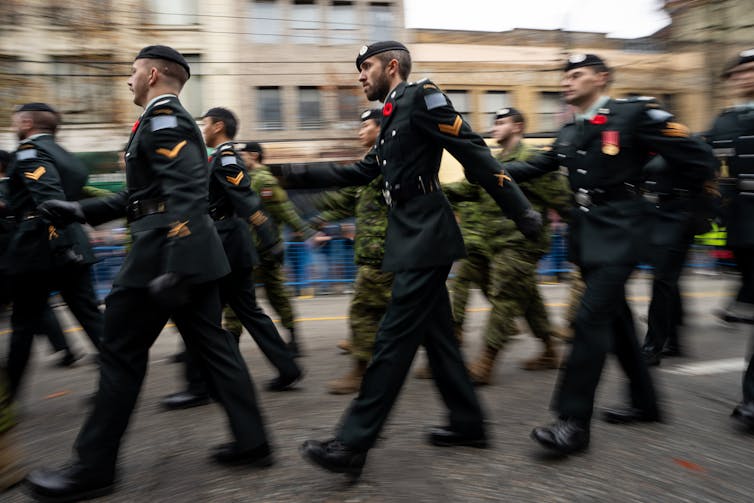 Foto de Blurri de grupos de personas con uniformes y boinas de color verde oscuro. Sus piernas muestran el movimiento del movimiento.