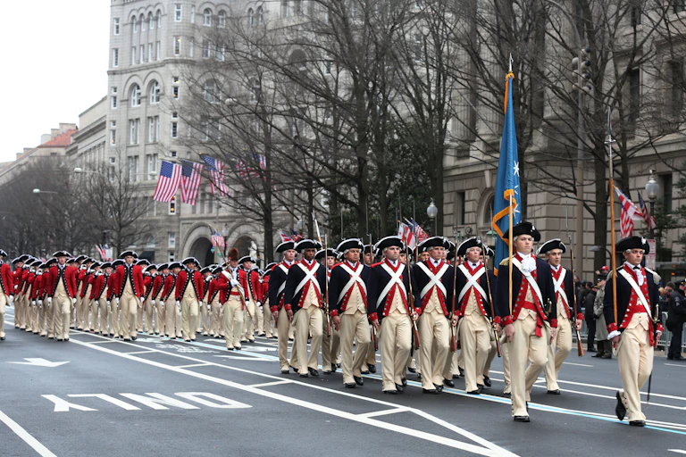 Men in red coats and white pants march along a road