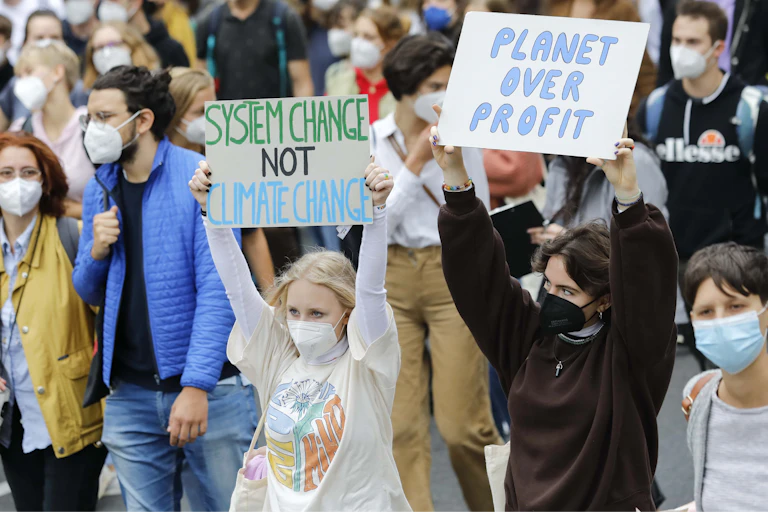 teenaged girls at protest hold placards reading system change not climate change and planet over profit