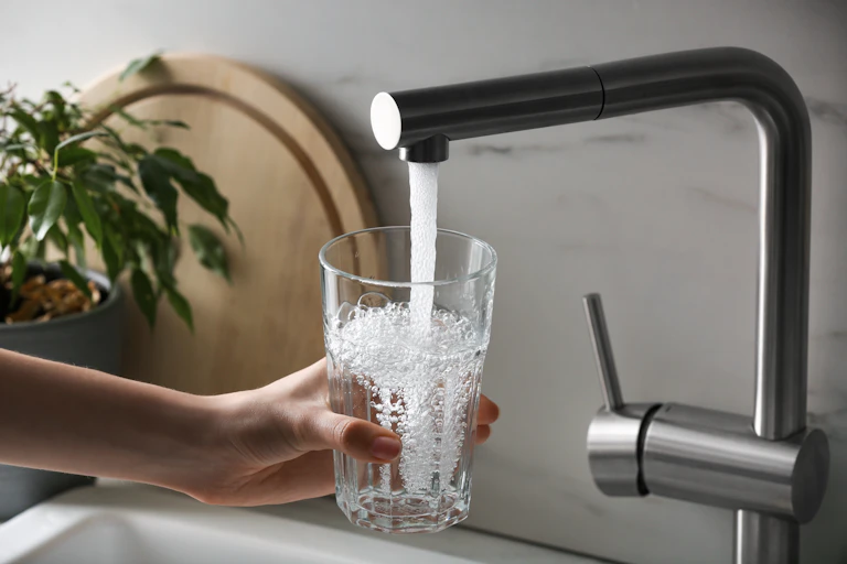 A hand filling a glass of water from a tap.