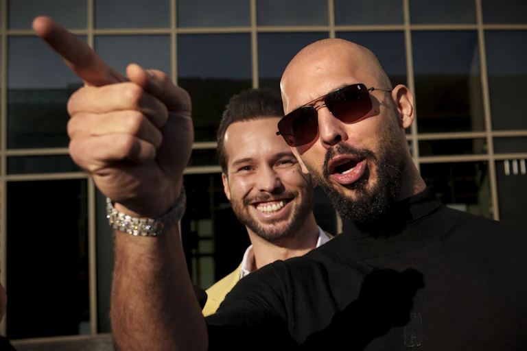 Andrew Tate frowns and points at the camera with his brother smiling behind him