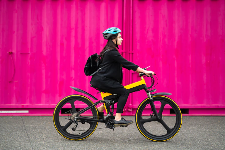 A woman riding an electric bicycle against a pink background.