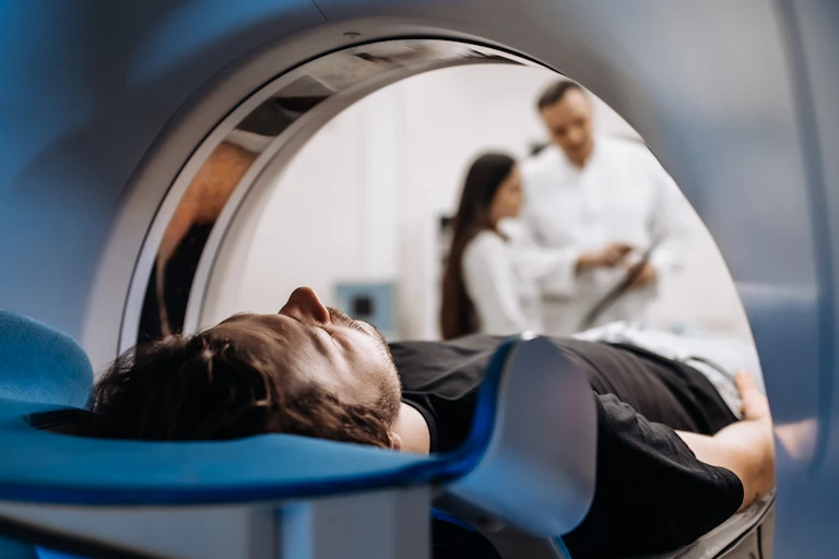 Man lying down in CT or MRI machine, two health workers consulting in background