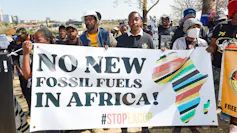 About 25 people stand with a banner that says 'No new fossil fuels in Africa!' and a large map of Africa