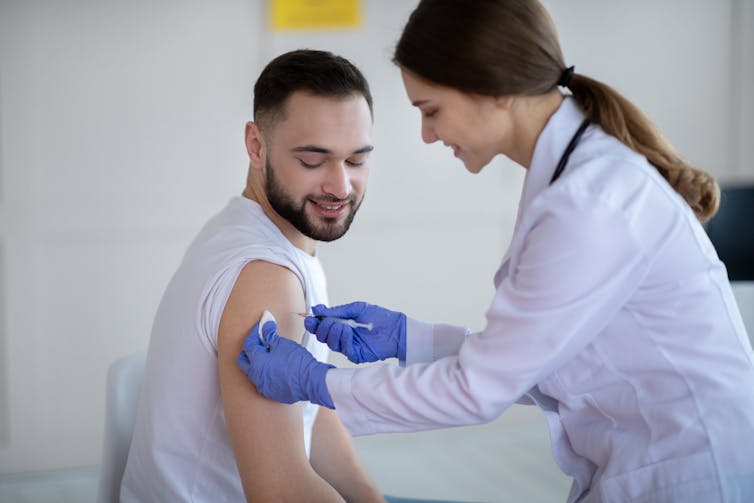 A young man receives a vaccine from a young female doctor.