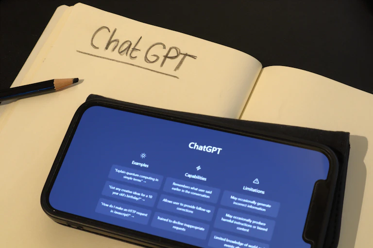 Móvil con las funciones de ChatGPT encima de un cuaderno donde se ha escrito a lápiz y subrayado "ChatGPT"