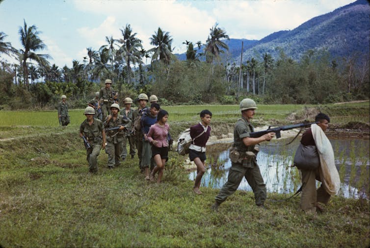 American soldiers leading Vietnamese citizens away during the Vietnam war.