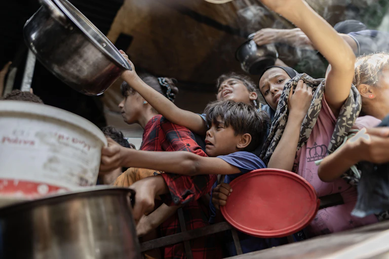 Children, some of them crying,hold out disches and bowls to receive food.