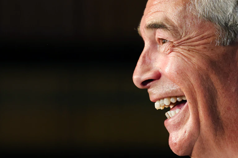 Close-up side view of a grinning Nigel Farage against a black background