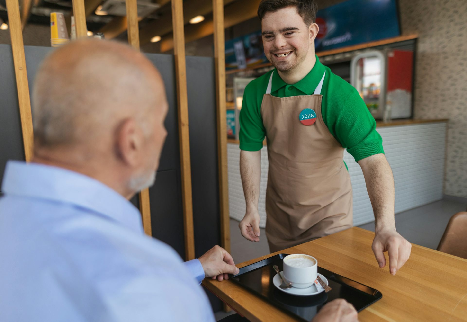 Un jeune employé trisomique sert un café à un client assis