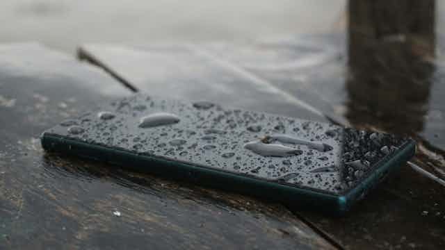 Smartphone sitting on table with rain splashes covering it