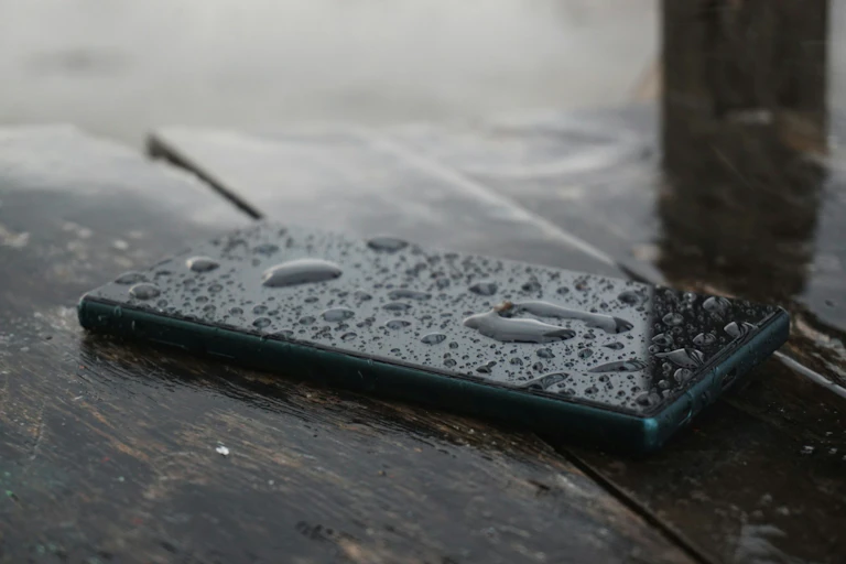 Smartphone sitting on table with rain splashes covering it