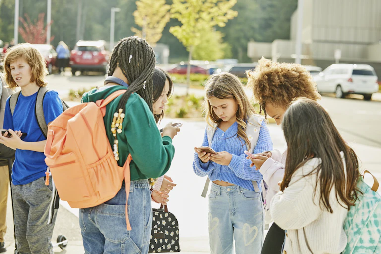 Middle school kids standing in a group outdoors on their smartphones