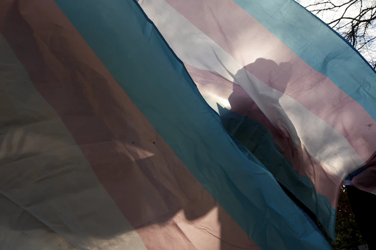 Silhouette of person against a trans flag outside
