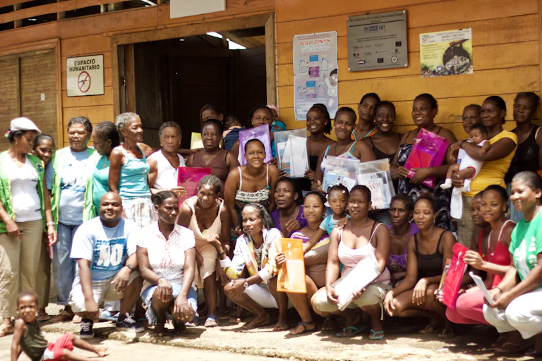 A group of about 30 women, as well as one man and some small children, pose for a photo outside a wooden building.