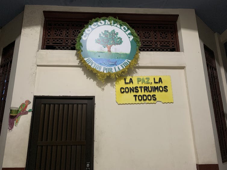 Two colorful signs, one of which has an image of a tree, hang on a white wall with a dark-colored door.