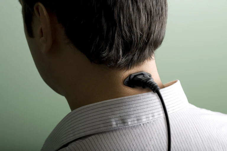 Back of a man's head with a plug going into his neck.