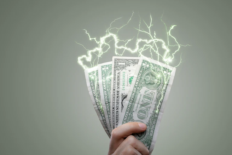 A hand holds dollar bills that are sparking with static electricity.