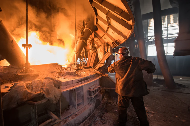 Man wearing a hard hat and protective clothing stoking a large furnace