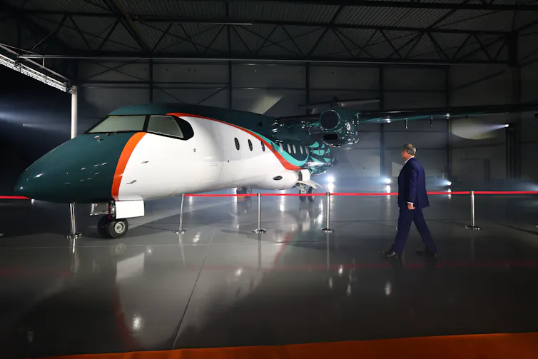 A man in a suit walks towards a sleek new German plane, designed to run on sustainable aviation fuel at the launch ceremony.