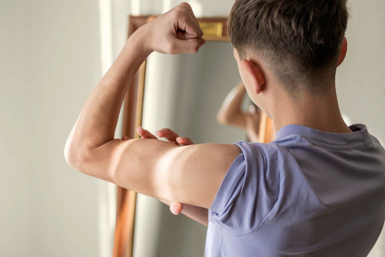 A teenage boy checks his bicep muscles in the mirror.