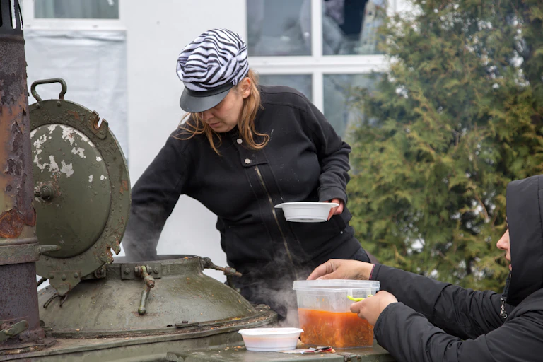 Una mujer con gorra saca comida de una gran olla