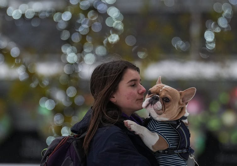 Una mujer joven con cabello largo y castaño con un bulldog bajo la lluvia.
