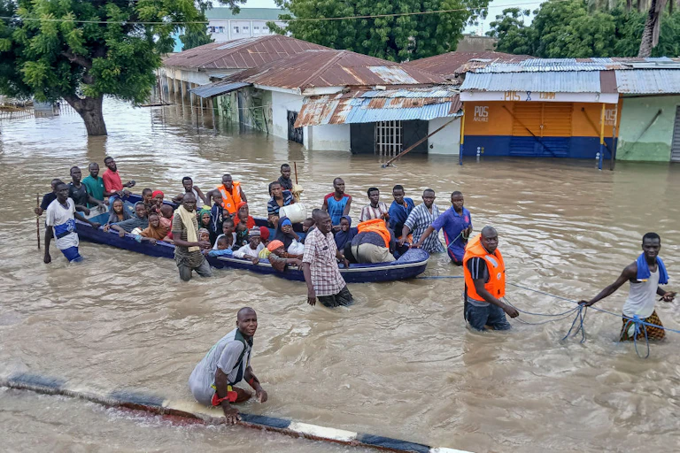 A flooded street with a boat full of people being guided by others who are wading in the water