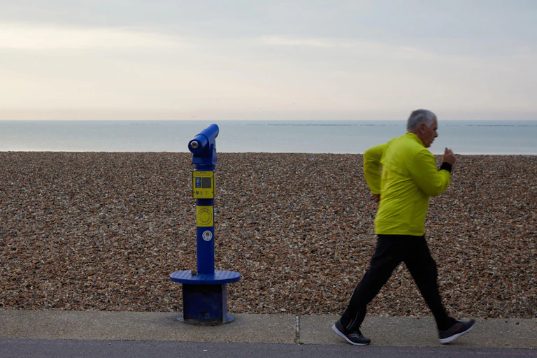 Older man walking fast along a beachfront.