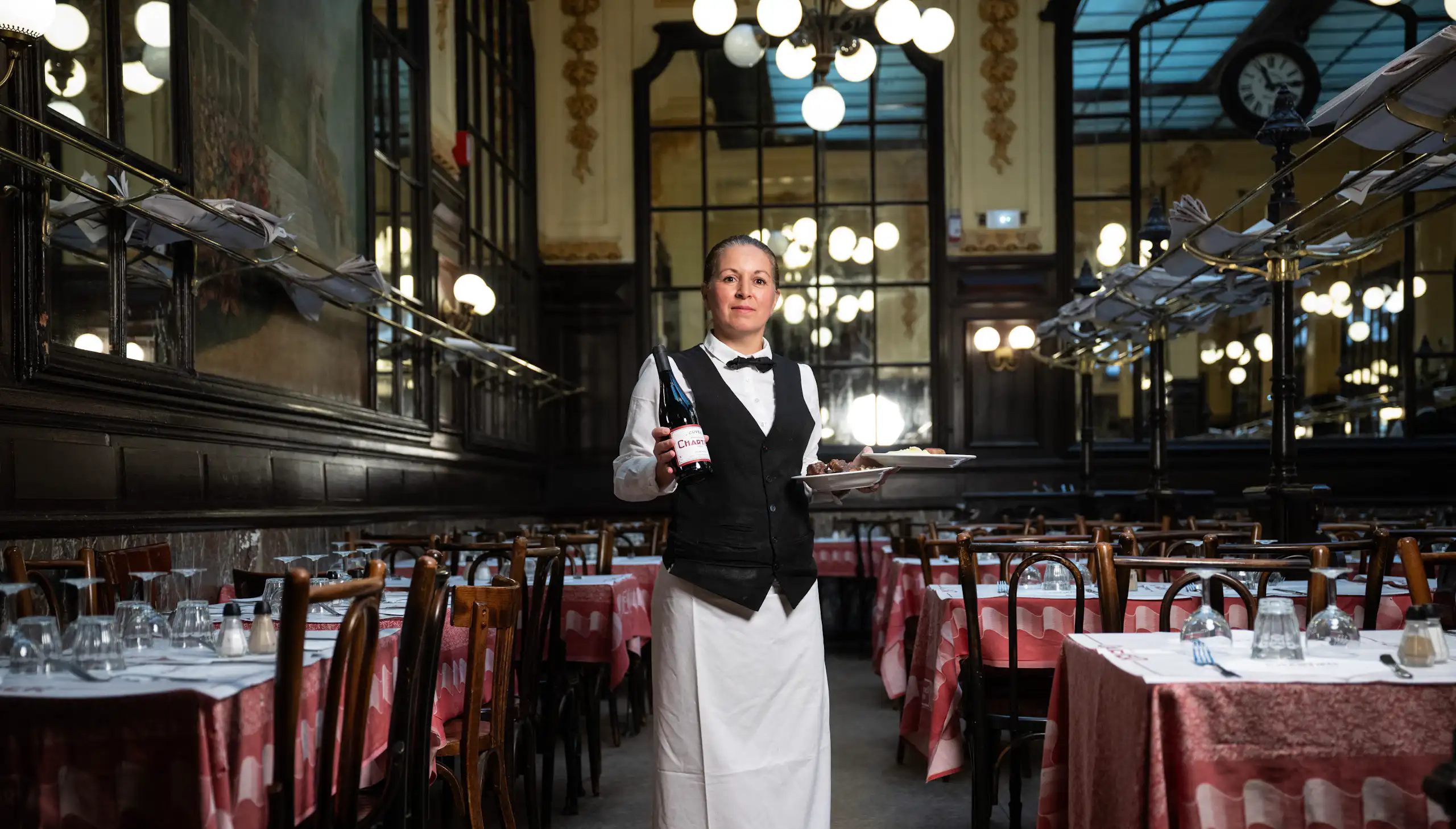 Portrait en pied de Fati, cheffe de rang Bouillon Chartier, posant dans la grande salle de son établissement.